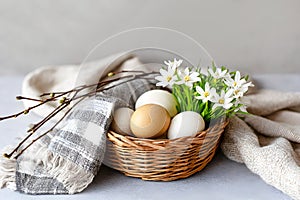 Easter basket with natural eggs and white flowers on cozy fabric background. Close-up photo