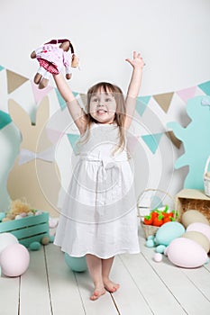 Easter! Beautiful little girl in a white dress rejoices at the holiday. Many different colorful Easter eggs, colorful interior. fa