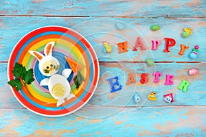 Easter breakfast idea for kids. Bunny rabbit made of boiled eggs on multicolored plate, blue wooden background