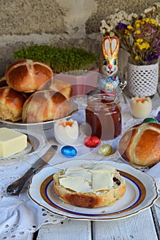 Easter breakfast with traditional hot cross buns, jam, butter and egg. Holiday still life. Festive table place setting decoration