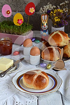 Easter breakfast with traditional hot cross buns, jam, butter and egg. Holiday still life. Festive table place setting decoration