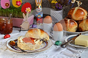 Easter breakfast with traditional hot cross buns, jam, butter and egg. Holiday still life. Festive table place setting decoration