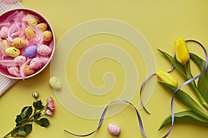 Easter bright background. Pink bowl with colorful eggs, pink feathers, spring flowers. Happy Easter concept. Post card