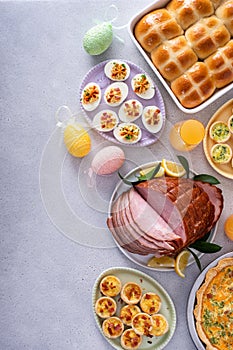Easter brunch on large table with spiral sliced ham, quiche, deviled eggs and hot cross buns