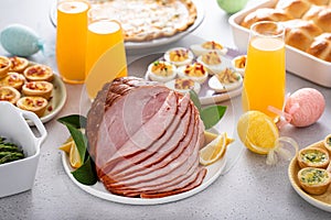 Easter brunch on large table with spiral sliced ham, quiche, deviled eggs and hot cross buns