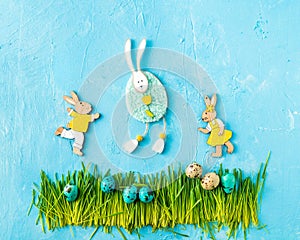 Easter bunnies figurines, painted eggs on green grass on blue background. Egg hunt creative concept