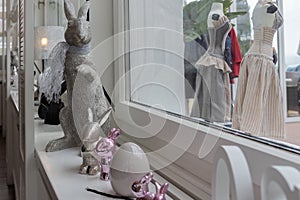 Easter bunnies sitting on sideboard in front of white bright window. Metal composition for Holiday.