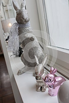 Easter bunnies sitting on sideboard in front of white bright window. Metal composition for Holiday concept