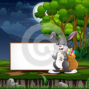 Easter bunny carrying a sack of easter eggs in front the blank sign
