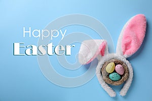 Easter bunny ears headband and dyed eggs in nest on blue background, flat lay