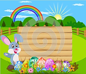 The Easter bunny holding a basket of Easter eggs with more Easter eggs and wood sign board