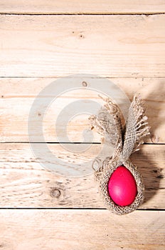 Easter bunny minimalist flat red chicken egg wrapped in burlap creative rabbit lies on a natural wooden background, top view,