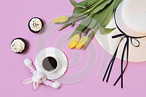 Easter bunny rabbit, coffee cup, white women`s hat and spring tulip flowers on pink background. Flat lay, copy space for text.