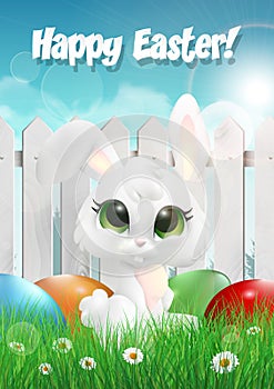 Easter bunny siting on a grass among Easter eggs, white wooden fence photo