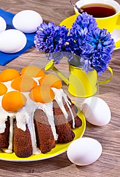 Easter cake with apricots on a yellow plate on a wooden background with blue flowers