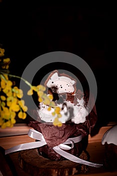 Easter cake in a brown package with an Easter bunny made of white icing sugar on a wooden background next to a sprig of mimosa.