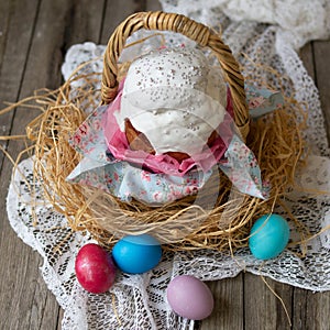 Easter cake - kulich.Traditional Easter sweet bread decorated white icing in straw basket and colored eggs on lace napkin on