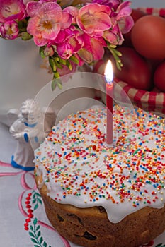 Easter cake with a lit candle, flowers, eggs and angel figurine