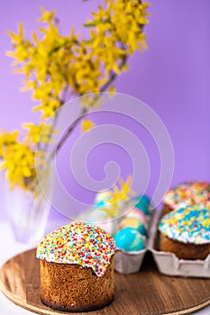 Easter cake on a purple background with yellow spring flowers. easter colored eggs. Easter food. minimal concept.
