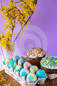 Easter cake on a purple background with yellow spring flowers. easter colored eggs. Easter food. minimal concept.