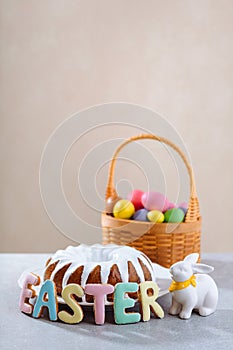 Easter cake surrounded by colorful cookies letters and rabbit and a basket full of colored eggs for the Easter holiday