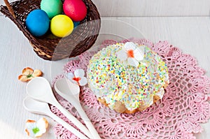 Easter cake on a table on a pink napkin, wooden spoons and a basket with colored eggs