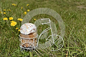 Easter cake in white glaze on a toy bike against green meadow. Symbol of festive spring season.Close up. Copy space