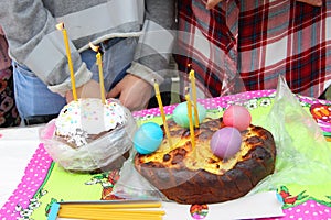 Easter cakes with a candle and colorful Easter eggs on background elements of human bodies without faces. Orthodox Easter,