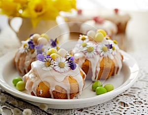 Easter cakes covered with icing decorated with spring and edible flowers and marzipan eggs on an Easter table.