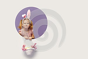 Easter card. Cute little child girl with bunny ears holding basket of Easter eggs. Child in a round hole circle in colored purple