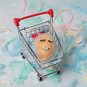 Easter card made of feathers and an egg with a painted cute face in an ER grocery basket