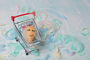 Easter card made of feathers and an egg with a painted cute face in an ER grocery basket