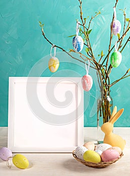 Easter card. White frame with copy space, twigs with spring leaves, color eggs on them on turquoise.