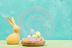 Easter card. Yellow bunny and decorative colorful eggs in wooden plate on turquoise Copy space.