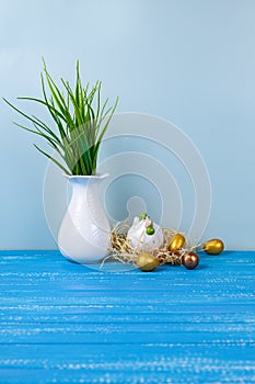 Easter chick in a nest and colorful eggs. White vase with a plant