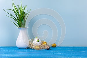 Easter chick in a nest and colorful eggs. White vase with a plant