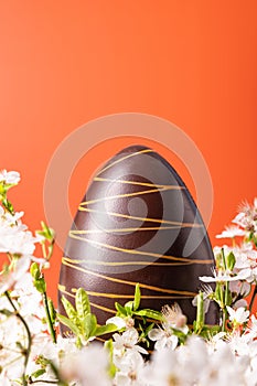 Easter chocolate egg with spring flowers on orange background
