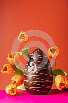 Easter chocolate egg with spring tulips on orange background