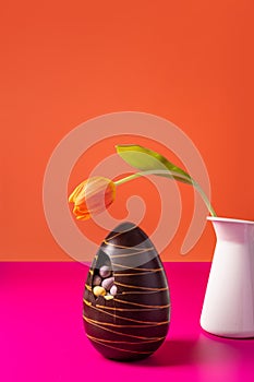 Easter chocolate egg with spring tulips on orange background