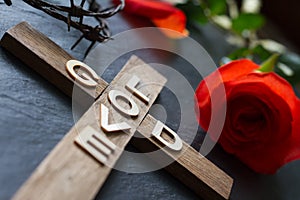 Easter christian wooden cross with an inscription god is love and red rose abstract religion background