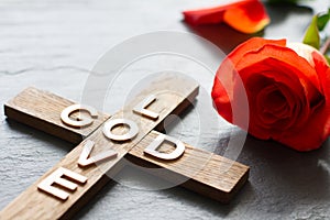 Easter christian wooden cross with an inscription god is love and red rose abstract religion background
