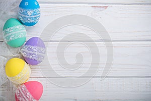 Easter colored eggs with lace ribbon on white wooden background