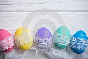 Easter colored eggs with lace ribbon on white wooden background photo