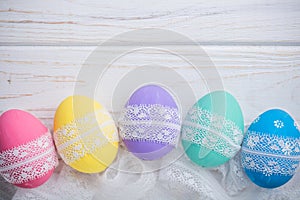 Easter colored eggs with lace ribbon on white wooden background photo