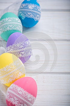Easter colored eggs with lace ribbon on white wooden background photo