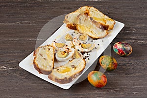 Easter colored eggs and sliced Easter bread in white plate on grey wooden board.