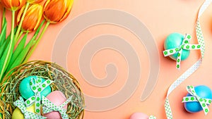 Easter Colorful egg with tape ribbon, spring tulips, white feathers on pastel pink background in Happy Easter decoration. Festive