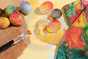 Easter colorful eggs with two painter brushes and a hand painted cloth,arranged on watercolor paper with yellow painted text.