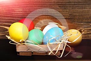 Easter colorful eggs in wooden basket with straw nest