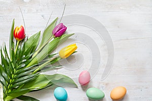 Easter colorful spring tulips with palm and eggs decoration on white wooden natural background